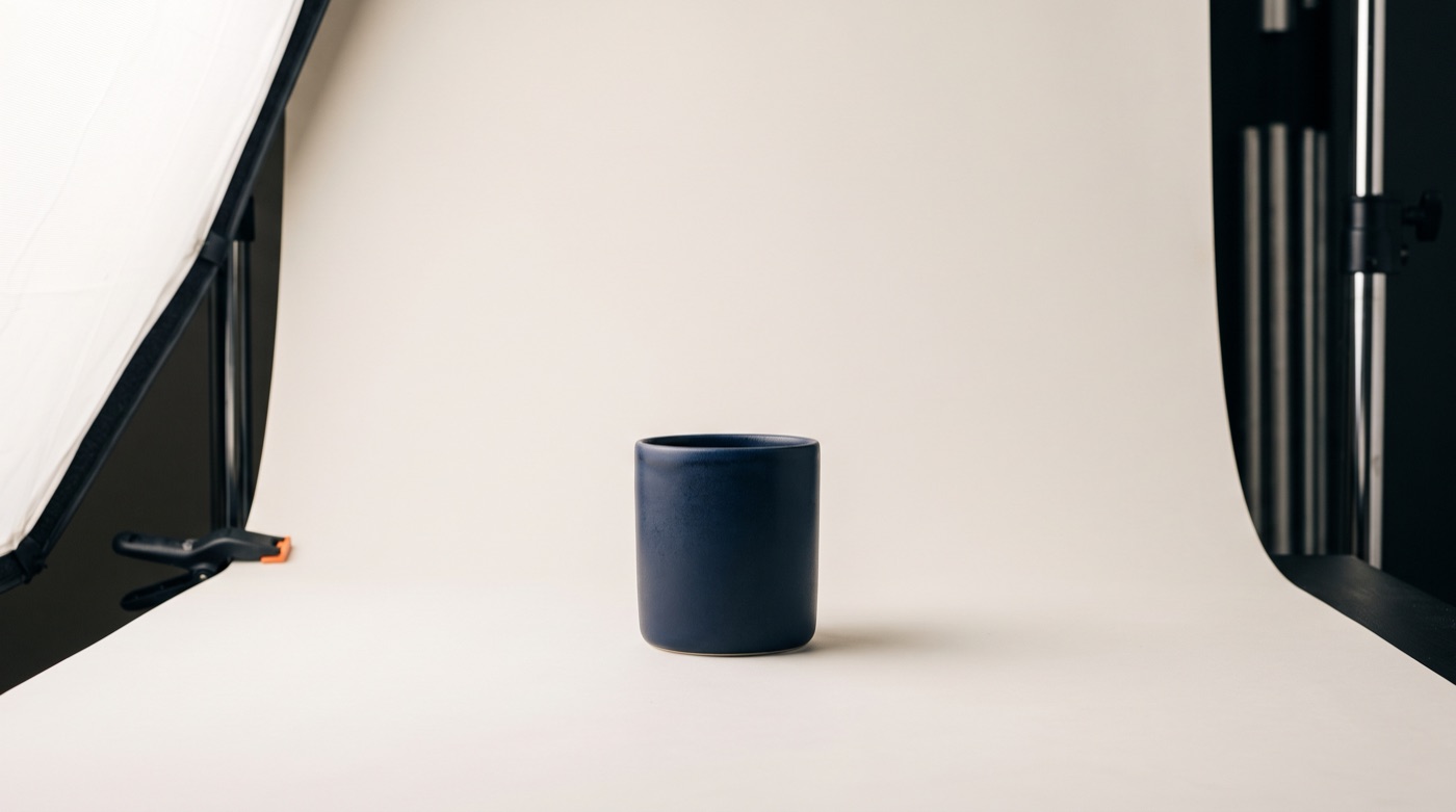 A navy ceramic cup on a seamless off-white backdrop in a softly lit product photography set